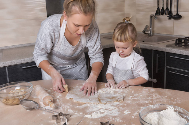 Happy family! A tiny daughter spends time with her mother in the kitchen to bake cookies. Mother's Day. - Zdjęcie, obraz