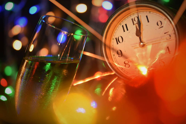 Новый год символ празднования; шампанское стекло фейерверк цвета света и часы лицо в одну минуту после полуночи
 - Фото, изображение