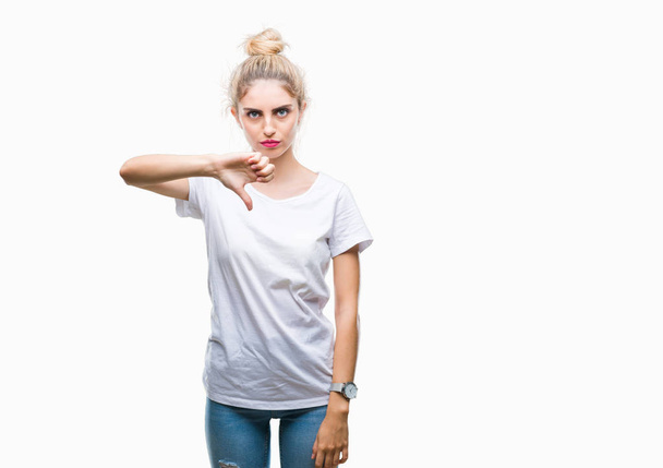 Young beautiful blonde woman wearing white t-shirt over isolated background looking unhappy and angry showing rejection and negative with thumbs down gesture. Bad expression. - Фото, зображення