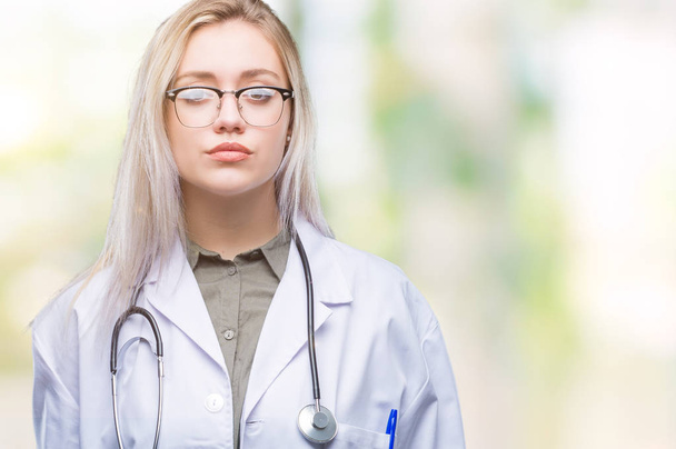 Young blonde doctor woman over isolated background with serious expression on face. Simple and natural looking at the camera. - Photo, image