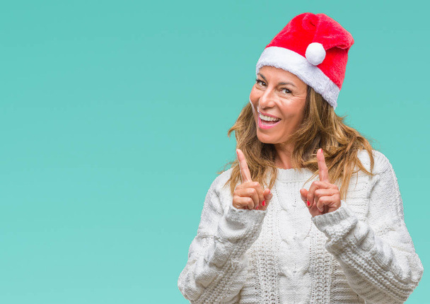 Középkorú vezető spanyol nő visel karácsonyi hat ujjal mutatva a fényképezőgép-val boldog és vicces arc elszigetelt háttérhez képest. Jó energia- és vibrafon. - Fotó, kép