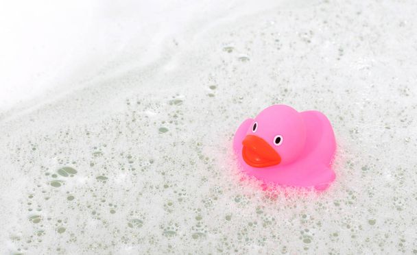 Roze eend in een badkuip, omgeven door zeep - Foto, afbeelding