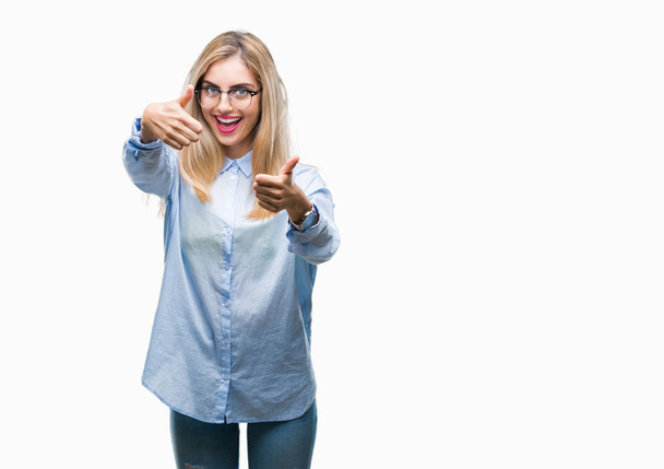 Young beautiful blonde business woman wearing glasses over isolated background approving doing positive gesture with hand, thumbs up smiling and happy for success. Looking at the camera, winner gesture. - Photo, image