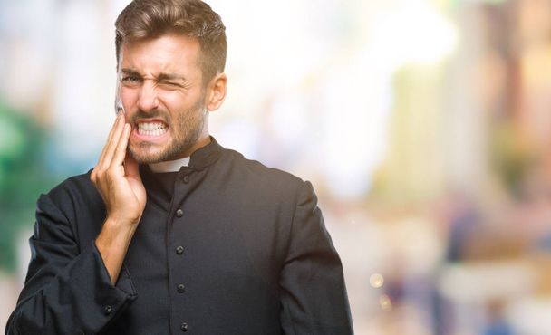 Jonge katholieke christelijke priester man over geïsoleerde achtergrond mond met de hand met pijnlijke expressie vanwege kiespijn of tandheelkundige ziekte op tanden aan te raken. Tandarts concept. - Foto, afbeelding