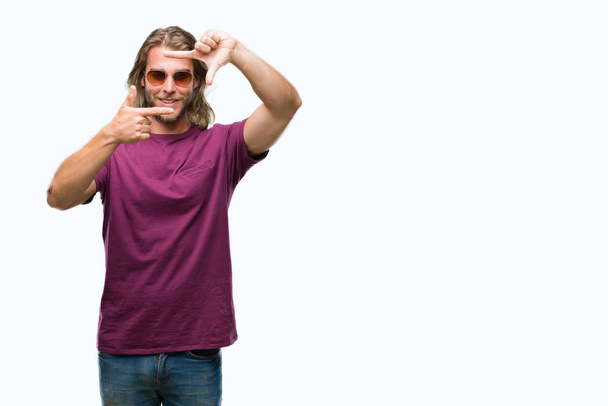 Young handsome man with long hair wearing sunglasses over isolated background smiling making frame with hands and fingers with happy face. Creativity and photography concept. - Zdjęcie, obraz