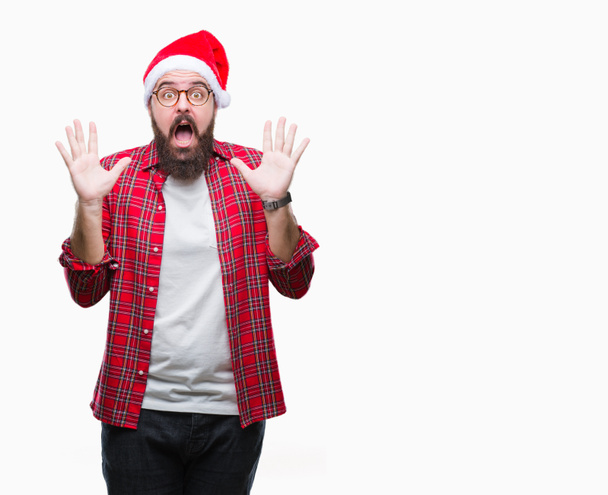 Young caucasian man wearing christmas hat over isolated background celebrating crazy and amazed for success with arms raised and open eyes screaming excited. Winner concept - Fotoğraf, Görsel