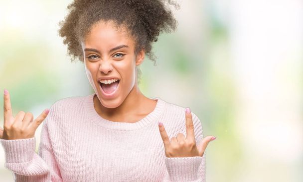 junge Afroamerikanerin trägt Winterpullover über isoliertem Hintergrund und schreit mit verrücktem Gesichtsausdruck Rock-Symbol mit erhobenen Händen. Musikstar. Schweres Konzept. - Foto, Bild