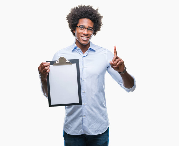 Афро-американец держит планшет на изолированном фоне, удивленный идеей или вопросом, указывая пальцем со счастливым лицом, номер один
 - Фото, изображение