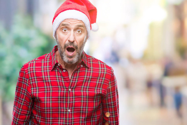 Старший чоловік середнього віку в різдвяному капелюсі над ізольованим фоном боїться і шокований з несподіваним виразом, страхом і збудженим обличчям
. - Фото, зображення