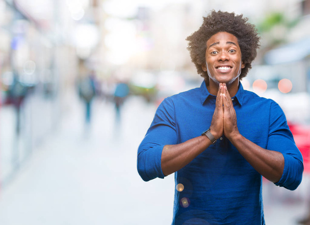 Αφρο αμερικανικό άνθρωπος πέρα από το απομονωμένο υπόβαθρο προσεύχεται με τα χέρια μαζί ζητώντας συγχώρεση χαμογελώντας αυτοπεποίθηση. - Φωτογραφία, εικόνα
