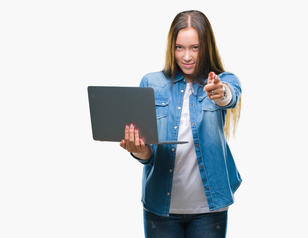 Nuori valkoihoinen nainen käyttää kannettavaa tietokonetta eristetyn taustan yli osoittaen sormella kameraa ja sinua, käsimerkki, positiivinen ja itsevarma ele edestä
 - Valokuva, kuva