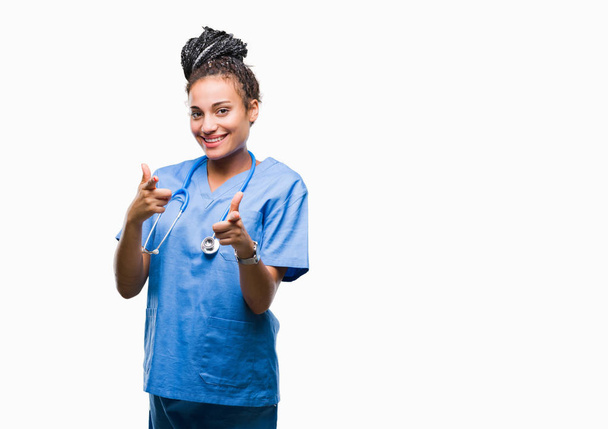 Νέοι πλεγμένες μαλλιών αφρικανικές αμερικανικές κορίτσι επαγγελματική χειρουργός πέρα από το απομονωμένο υπόβαθρο επισημαίνοντας δάχτυλα κάμερα με πρόσωπο χαρούμενο και αστείο. Καλή ενέργεια και τα vibes. - Φωτογραφία, εικόνα