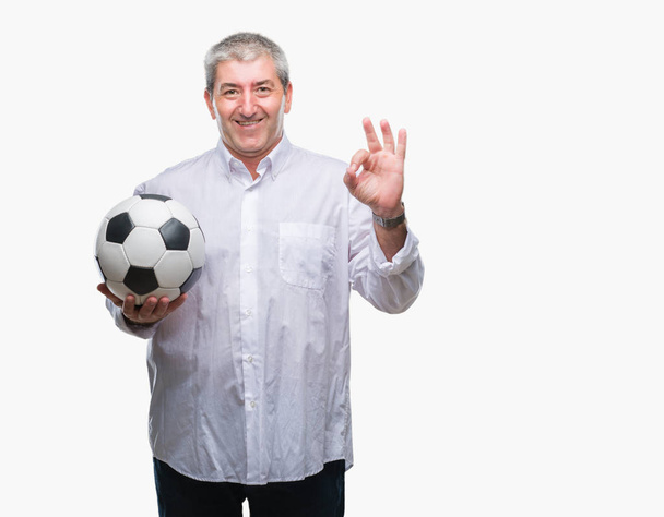 Bello uomo anziano che tiene palla da calcio su sfondo isolato facendo ok segno con le dita, simbolo eccellente
 - Foto, immagini