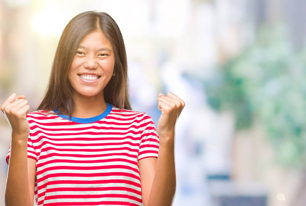 Jeune femme asiatique sur fond isolé très heureuse et excitée faisant geste gagnant avec les bras levés, souriant et criant pour le succès. Concept de célébration
. - Photo, image