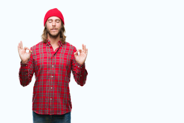 Young handsome man with long hair wearing red cap over isolated background relax and smiling with eyes closed doing meditation gesture with fingers. Yoga concept. - Photo, image
