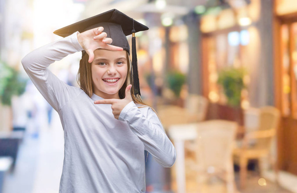 Young beautiful girl wearing graduate cap over isolated background smiling making frame with hands and fingers with happy face. Creativity and photography concept. - Photo, Image