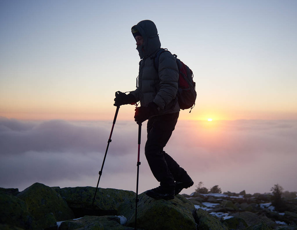 Sylwetka turysta turystyka wycieczkowicz człowieka z plecaka i kije trekingowe na szczyt góry skaliste mgliste chmury na backgrond - Zdjęcie, obraz