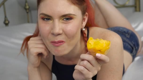 Redhead woman eats fresh fruit while lying in bed. healthy breakfast. slow motion - Felvétel, videó