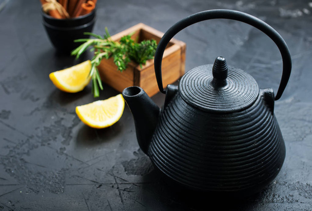 close up view of black teapot, mint, lemon pieces and cinnamon sticks on dark tabletop - Photo, image