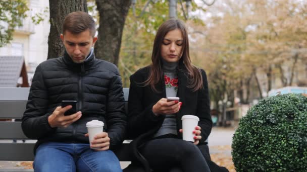 Φίλοι σερφάρισμα στο internet, πίνοντας καφέ και να μιλάμε, ενώ κάθεται σε ένα παγκάκι, σε δρόμο - Πλάνα, βίντεο