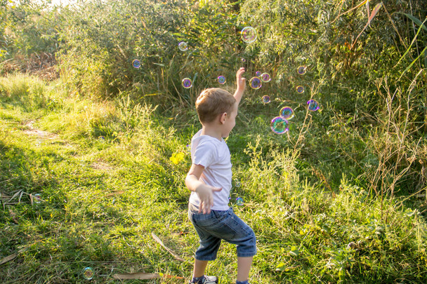 Ξανθό αγόρι, παίζοντας, χορεύοντας και διασκεδάζοντας στη φύση στο τζιν σορτς και άσπρο t-shirt - Φωτογραφία, εικόνα