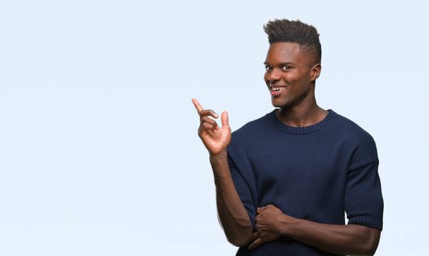 Νεαρός αφρικανική αμερικανική άνθρωπος πέρα από το απομονωμένο υπόβαθρο με ένα μεγάλο χαμόγελο στο πρόσωπό του, δείχνοντας με το χέρι και το δάκτυλο στην πλευρά που βλέπει η κάμερα. - Φωτογραφία, εικόνα