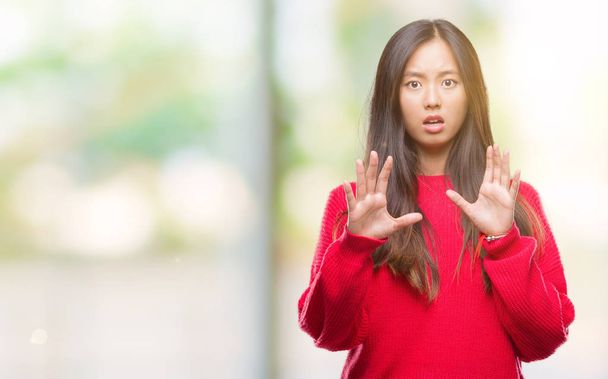 Giovane donna asiatica indossa maglione invernale su sfondo isolato spaventato e terrorizzato con espressione di paura fermare il gesto con le mani, gridando in stato di shock. Concetto di panico
. - Foto, immagini