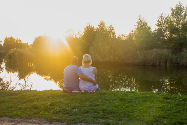 Happy couple in love sitting on the bank of the lake in the forest in the rays of the setting sun - Photo, Image