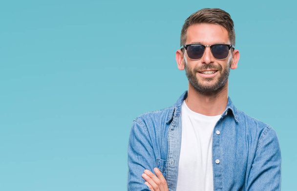 Ein junger gutaussehender Mann mit Sonnenbrille über einem einsamen Hintergrund lächelt glücklich mit verschränkten Armen in die Kamera. positive Person. - Foto, Bild