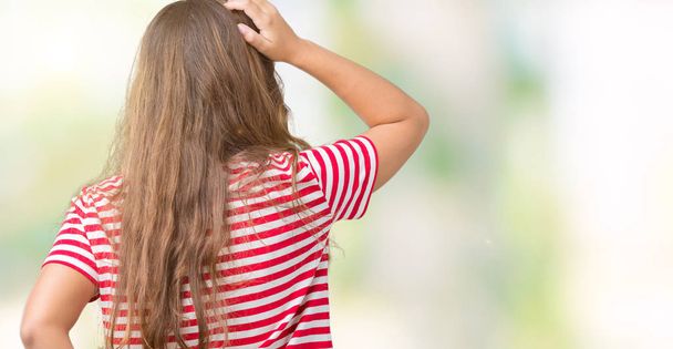 Young beautiful brunette woman wearing stripes t-shirt over isolated background Backwards thinking about doubt with hand on head - Zdjęcie, obraz