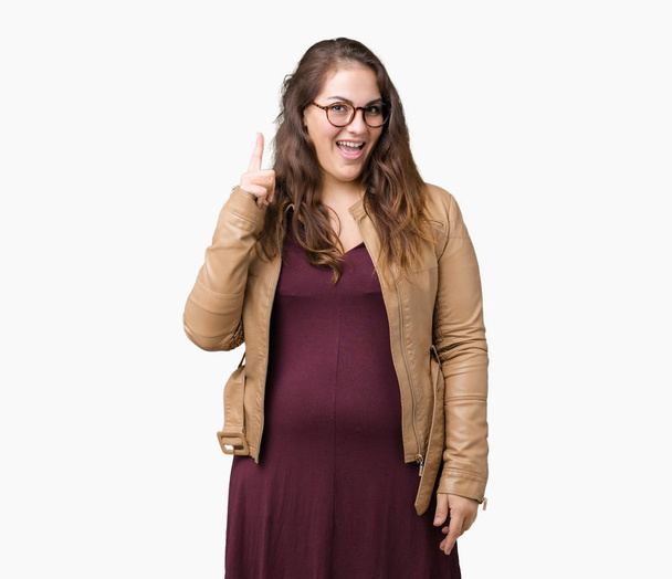 Beautiful plus size young woman wearing a dress and leather jacket over isolated background pointing finger up with successful idea. Exited and happy. Number one. - Foto, afbeelding