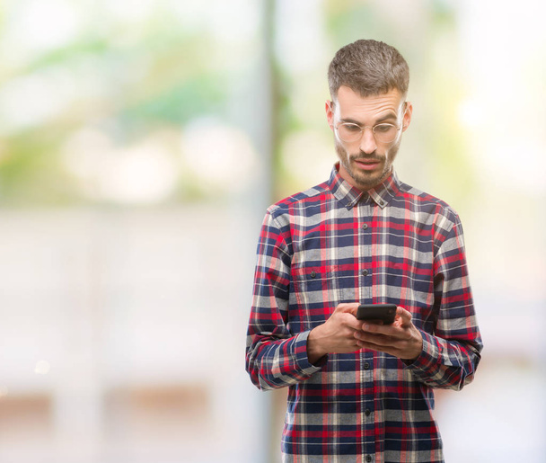 Young hipster adult man holding smartphone scared in shock with a surprise face, afraid and excited with fear expression - Photo, Image