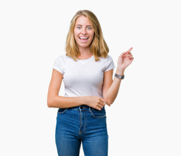 Beautiful young woman wearing casual white t-shirt over isolated background with a big smile on face, pointing with hand and finger to the side looking at the camera. - Photo, Image