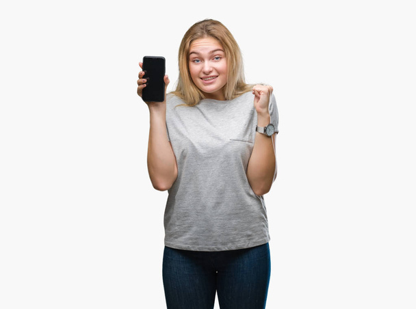 Mujer caucásica joven mostrando la pantalla del teléfono inteligente sobre fondo aislado gritando orgulloso y celebrando la victoria y el éxito muy emocionado, animando emoción
 - Foto, imagen