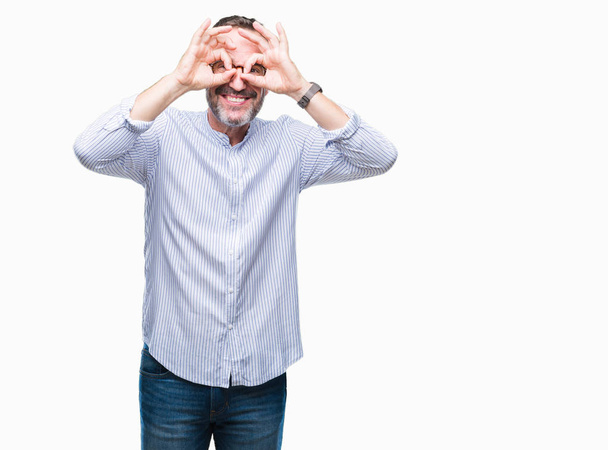 Hombre de mediana edad con gafas sobre un fondo aislado haciendo un buen gesto como prismáticos sacando la lengua, ojos mirando a través de los dedos. Expresión loca
. - Foto, imagen