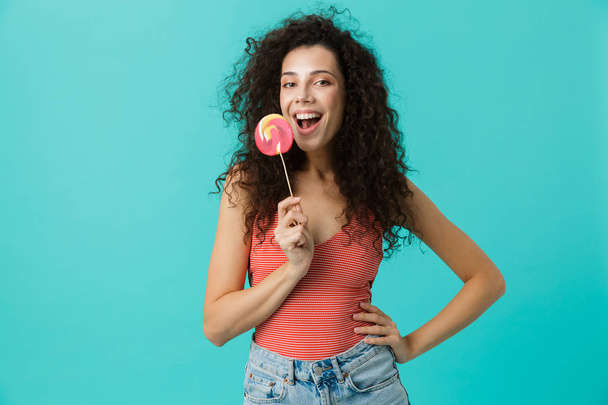 Portrait of gorgeous woman 20s wearing casual clothing holding lollipop isolated over blue background - Фото, изображение