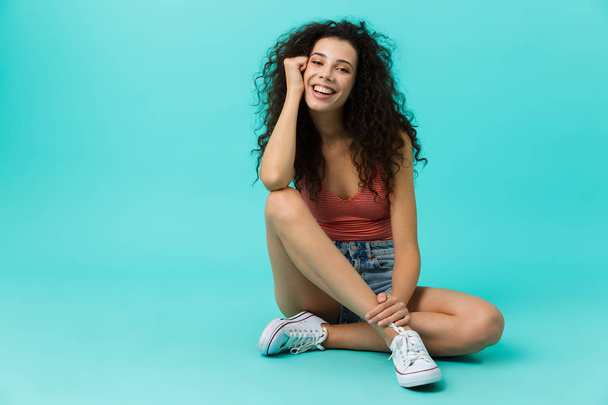 Image of seductive woman 20s wearing casual clothing laughing while sitting on floor with legs crossed isolated over blue background - Fotoğraf, Görsel