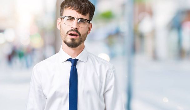 Νέοι επαγγελματίες όμορφος άνθρωπος φορώντας γυαλιά πέρα από το απομονωμένο υπόβαθρο στο πρόσωπό του σοκ, ψάχνει δύσπιστος και σαρκαστική, εξέπληξε με ανοιχτό το στόμα - Φωτογραφία, εικόνα