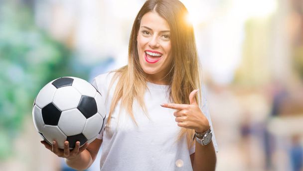 Jonge mooie vrouw houdt van voetbal over geïsoleerde achtergrond erg blij met de hand en de vinger te wijzen - Foto, afbeelding
