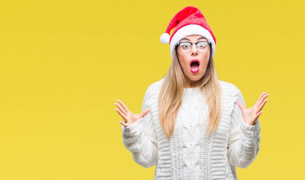 Giovane bella donna indossa cappello di Natale su sfondo isolato pazzo e pazzo urlando e urlando con espressione aggressiva e braccia alzate. Concetto di frustrazione
. - Foto, immagini