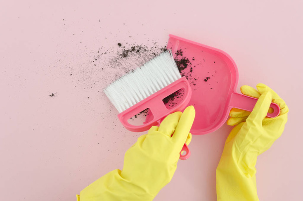 Flat lay photography female hands in yellow latex gloves with brush and dustpan clean the dirt on pink background. Copy space. Mock up. Top view. - Photo, Image