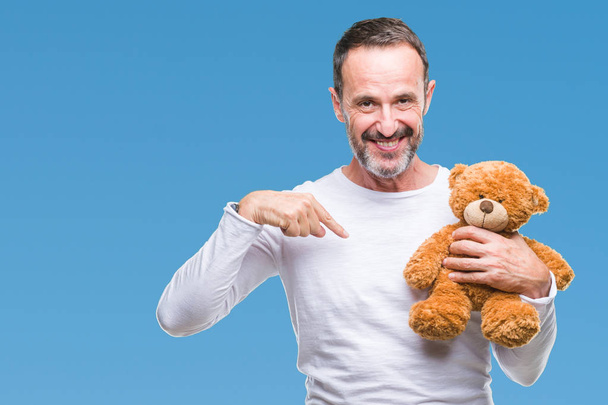 Middle age senior hoary man holding teddy bear over isolated background with surprise face pointing finger to himself - Fotó, kép
