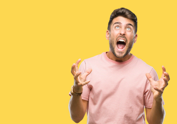 Young handsome man over isolated background crazy and mad shouting and yelling with aggressive expression and arms raised. Frustration concept. - Photo, Image