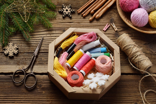 Gift wrapping. Present for the needlewoman - thread, floss, needles, hook, cotton yarn. Composition with box, festive decoration and fir tree branch. Merry Christmas and Happy New Year concept. - Photo, Image