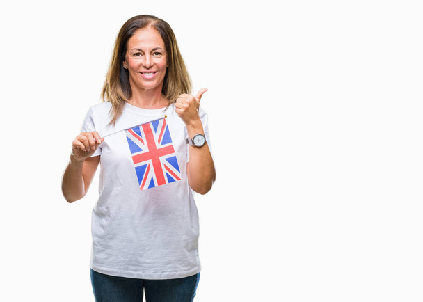 Mulher hispânica de meia idade segurando bandeira do Reino Unido sobre fundo isolado feliz com grande sorriso fazendo sinal ok, polegar com os dedos, excelente sinal
 - Foto, Imagem