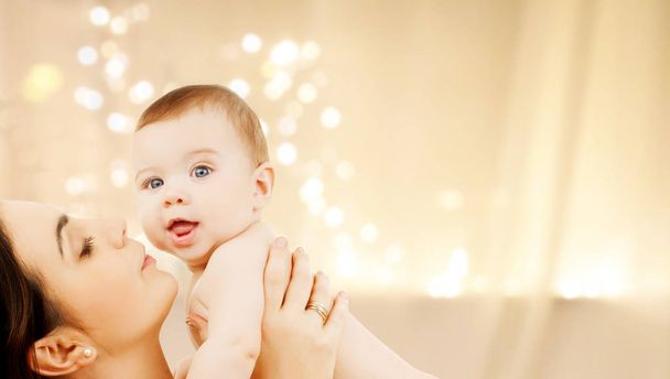 mãe beijando bebê sobre luzes de Natal
 - Foto, Imagem