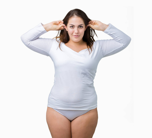 Beautiful plus size young overwight woman wearing white underwear over isolated background Smiling pulling ears with fingers, funny gesture. Audition problem - Photo, Image