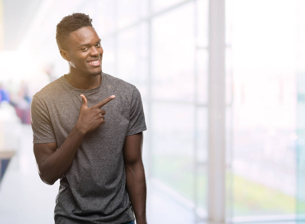 Young african american man wearing grey t-shirt cheerful with a smile of face pointing with hand and finger up to the side with happy and natural expression on face looking at the camera. - Foto, Imagen