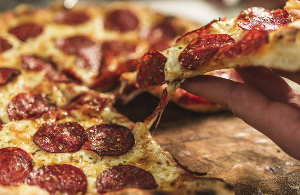 heiße Pizza mit schmelzendem Käse und Peperoni auf einem rustikalen Holztisch - Foto, Bild