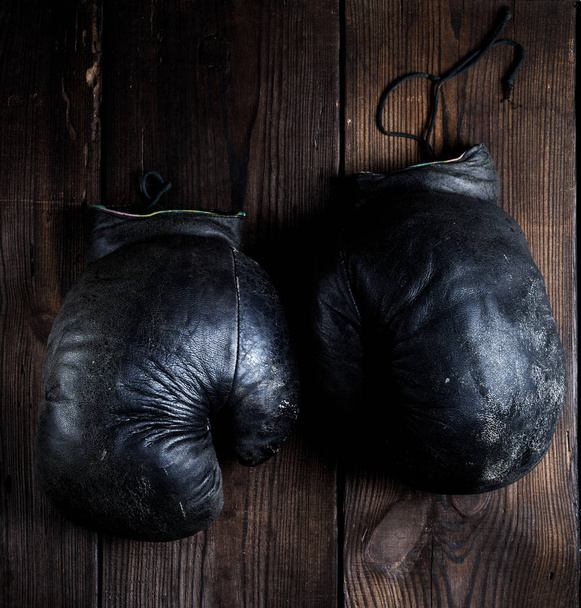 zeer oude zwarte bokshandschoen voor beginners op een bruin houten achtergrond, bovenaanzicht - Foto, afbeelding